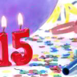 red lit birthday candles that spell out "15" with streamers, a balloon, and a party horn in the background