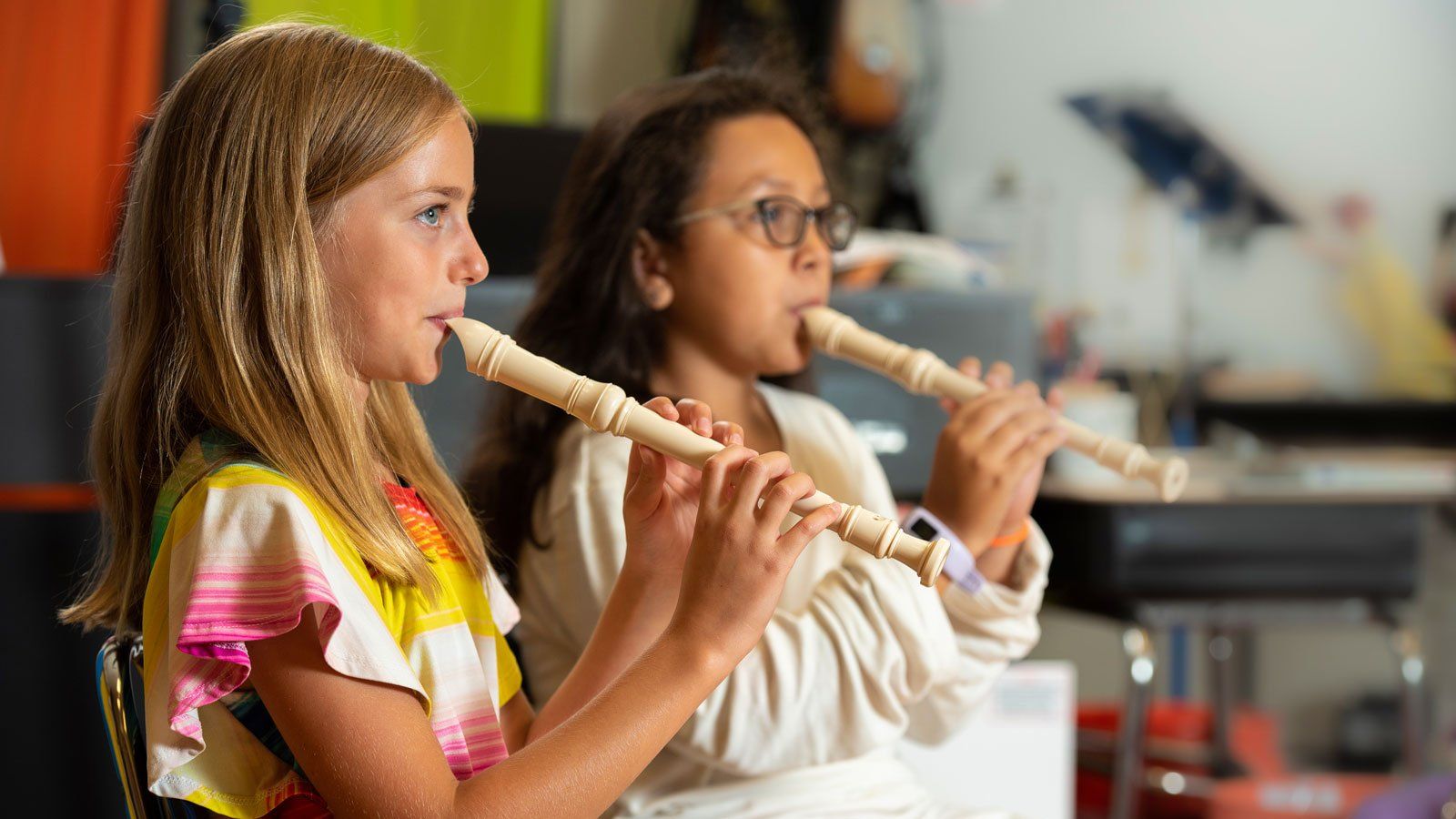Two girls playing recorders and paying attention to music teacher
