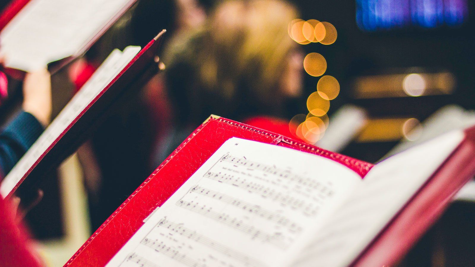 Sheet music on red notebook in foreground with warm blurred bokeh in background