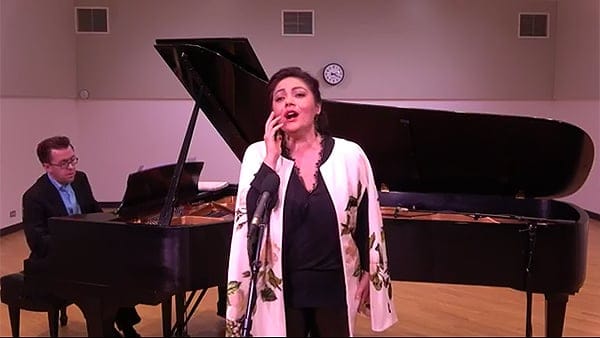 Wearing a black dress and white shawl, Ailyn Pérez performs in front of a piano in the WFMT studios