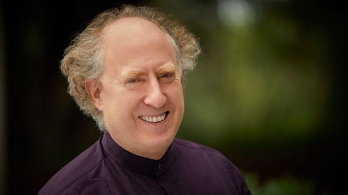 Pianist Jeffrey Kahane gives a smile in front of a green, natural background