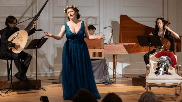 Nathalie Colas in dark emerald gown on stage singing with harpsichord, cello, and theorbo accompaniment.