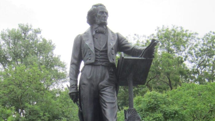 Detail of statue of Felix Mendelssohn against a bright backdrop and a row of green trees