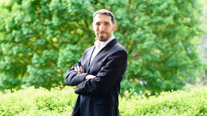 Portrait of Jonathan Leshnoff, dressed in a suit, in front of a green tree