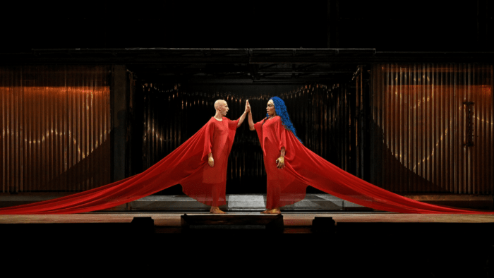 Akhnaten and Nefertiti identically dressed in red gowns, symmetrical image, touching hands.