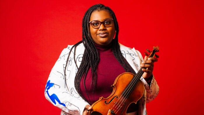 Caitlin Edwards holds a violin against a vivid red background