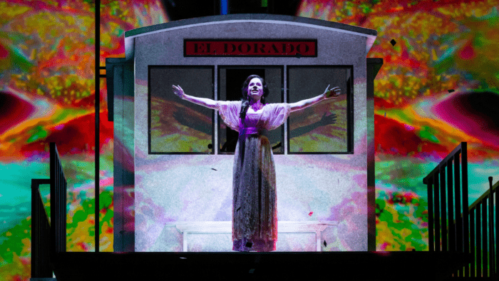 Ana María Martínez as Florencia, center stage, arms outstretched, colorful background.