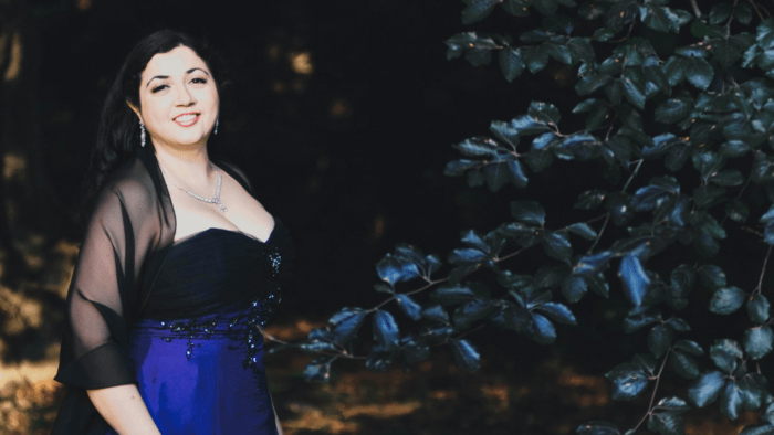 Portrait of Sherezade Panthaki in black and blue gown, organza wrap over shoulders, dark forest setting