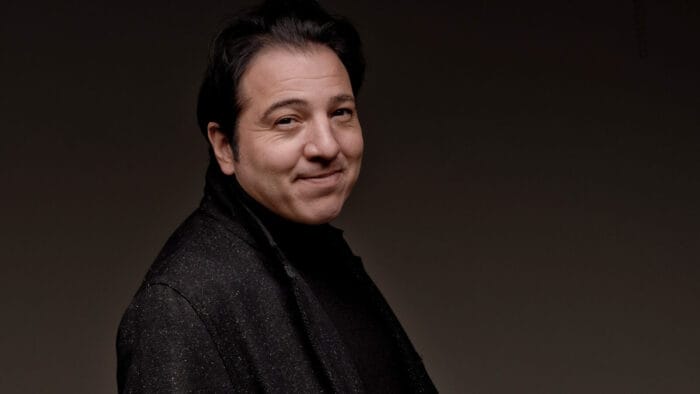 Fazıl Say, in a dark overcoat, gives a closed-mouth smile in front of a dark background