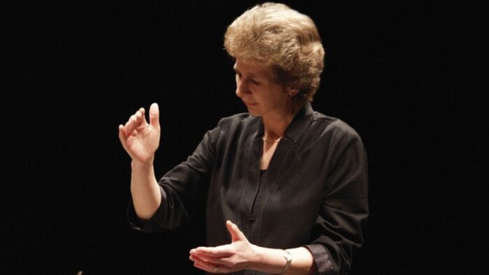 Jane Glover in black blouse with sleeves rolled to elbow looking to the bottom left corner, hands in a conducting gesture