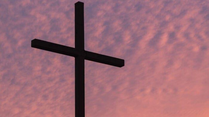 a cross stands in silhouette against a cloudy, sunset sky