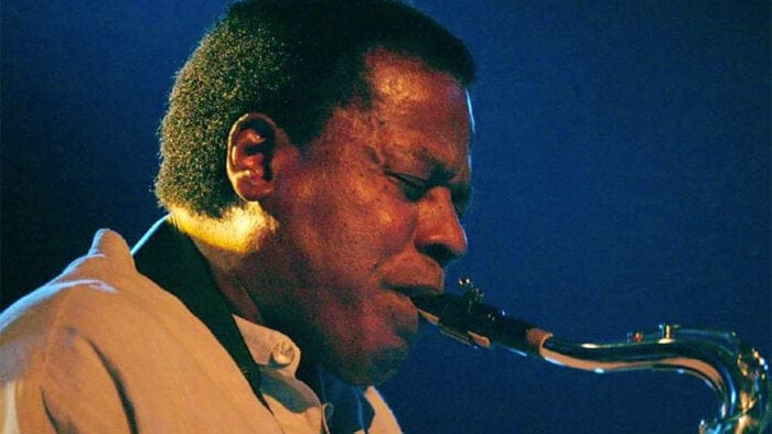 Wayne Shorter, in a close up, mesmerizing in a saxophone performance against a blue backgorund