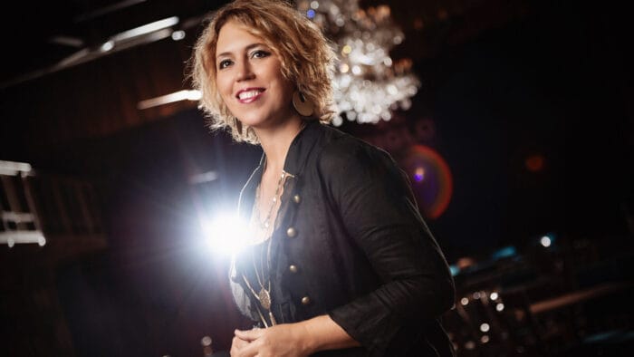 pianist and composer Gabriela Montero beams, with a chandelier and spotlight behind her