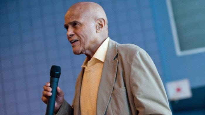 Harry Belafonte holds a microphone in front of a blue wall