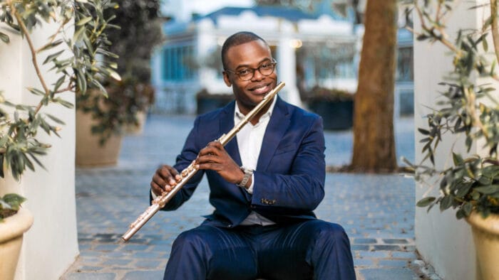 Demarre McGill, seated outside, smiles at the camera while holding the flute