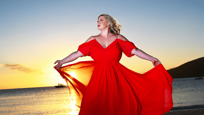 Laura Strickling in a flowing red gown on a beach at sunset