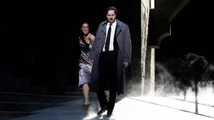 Peter Mattei (as Don Giovanni) struts ragefully in a black suit and tie and trench coat, with Federica Lombardi (as Donna Anna) following behind in a nightgown