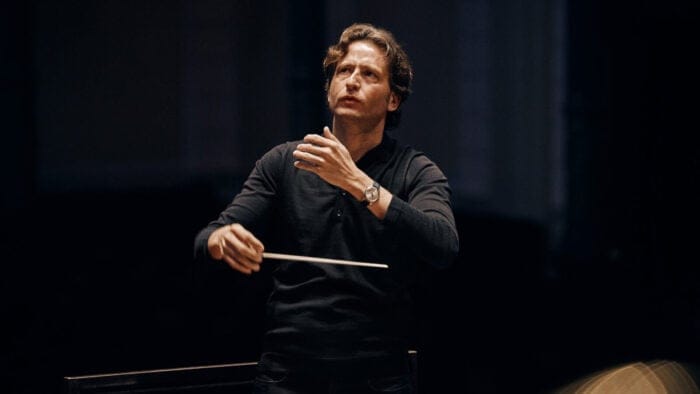 Gustavo Gimeno conducting in a dark shirt in front of a dark shirt