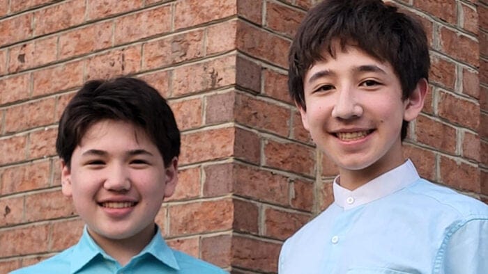Brothers Joseph and Samuel Kim, both dressed in blue, pose together in front of a brick wall
