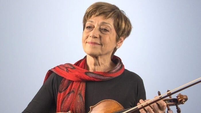 Miriam Fried, wearing a black dress and a red scarf, poses with a violin and bow