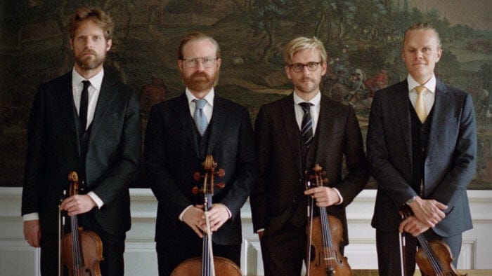 The Danish String Quartet poses in suits in front of a landscape fresco