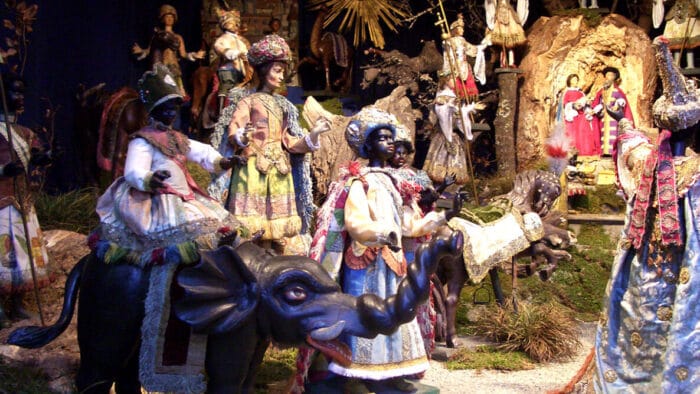 Visitors to a manger, one on an elephant, offer gifts to a newborn.