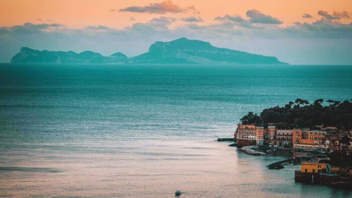 a serene view of rustic buildingg, the sea, and a faraway island off the coast of Naples