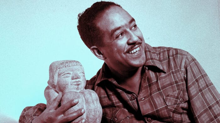 Langston Hughes, smiling, poses with a small stone sculpture