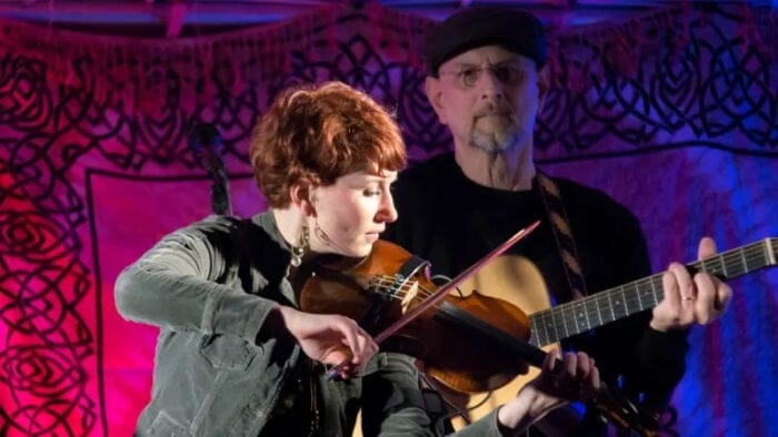 woman fiddler with guitar player in background
