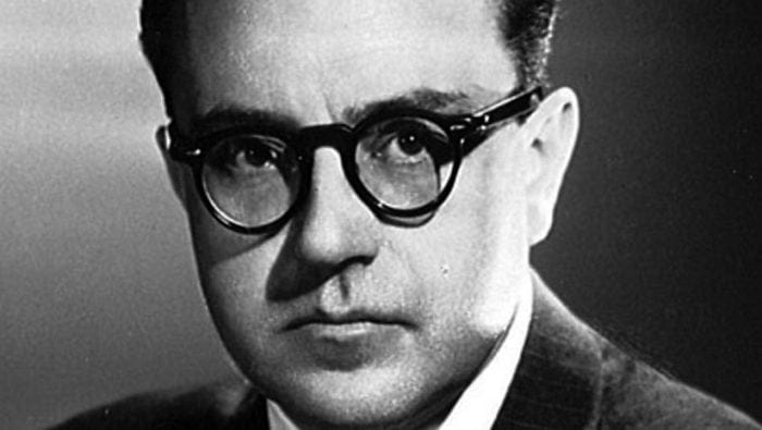 a tight photo closeup of Alberto Ginastera, a stern looking man in a suit and thick black glasses, black and white