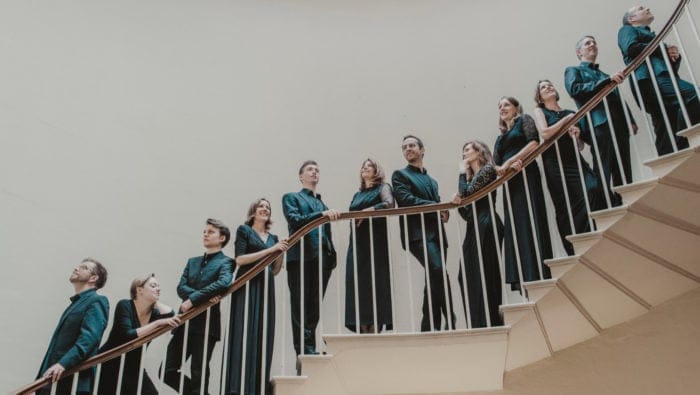 Musicians dressed in black pose on a stairwell against a gray background