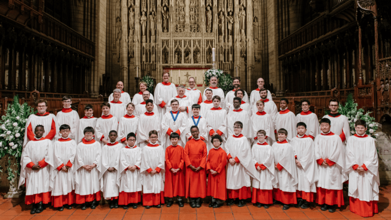 The Saint Thomas Choir of Men and Boys portrait at St Thomas Church, New York. The boys and men in red cassocks and white surplices posed in front of the organ; three boys front row center are not wearing surplices.