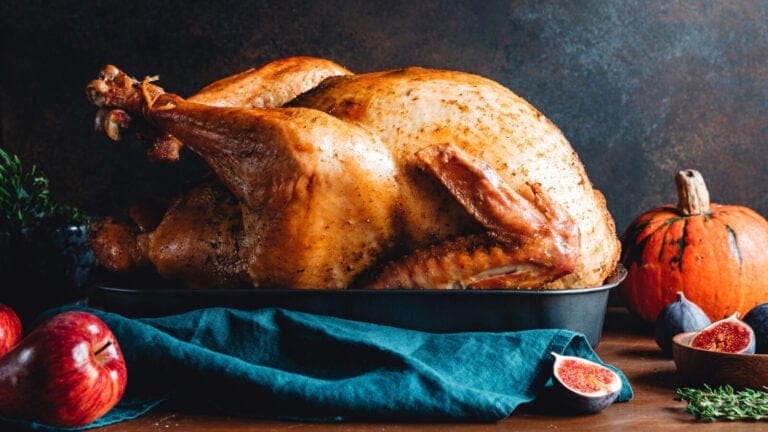 a rustic table holds a roast turkey, a pumpkin, and some fruit