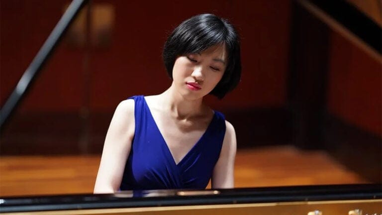 Jiao Sun seated at the piano in a blue dress