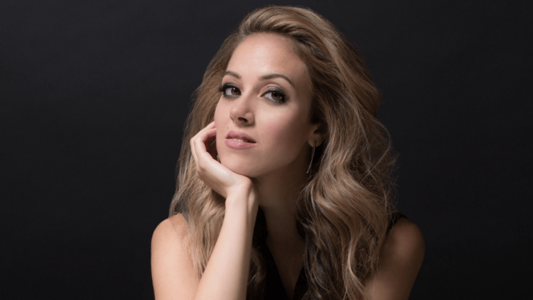 Portrait of Lauren Snouffer, chin resting on right palm, fingers touching her right cheek, dark background.