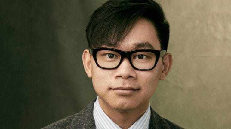 Viet Cuong, in thick black glasses and a casual suit and striped blue oxford shirt, gives a small style in a studio photo portrait