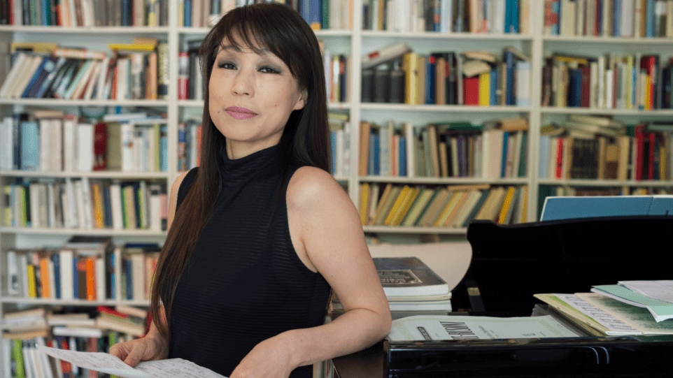 Composer Unsuk Chin poses in her study, with a piano and bookshelves in the background