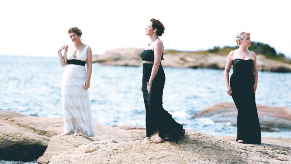 Three singers dressed elegantly on a beach