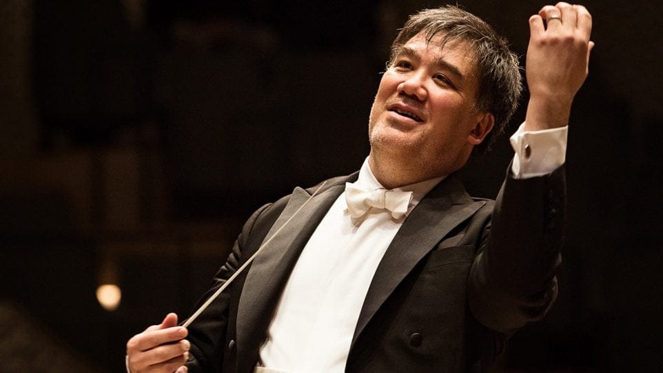 Alan Gilbert onstage, conducting with a slight smile