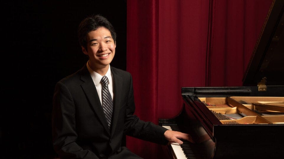 Tyler Wang, a young pianist, poses at the keyboard with a red curtain in the background