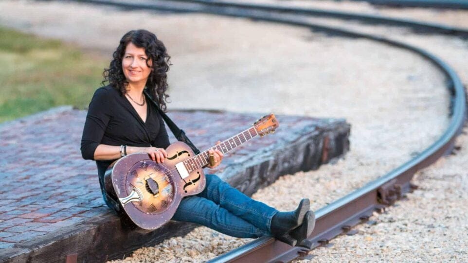 woman with guitar sits along train tracks