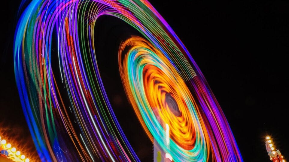 Bright, vibrant light trails of a ferris wheel in motion against a dark night sky