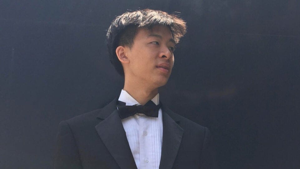Samuel Lam wears a tux and poses outside against a black wall