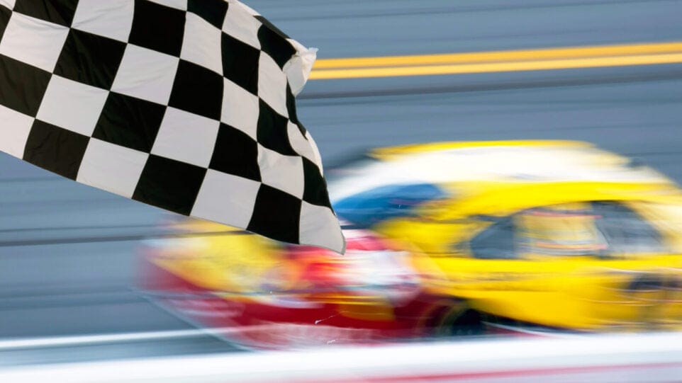a yellow and red car zooms past a waving black and white checkered flag