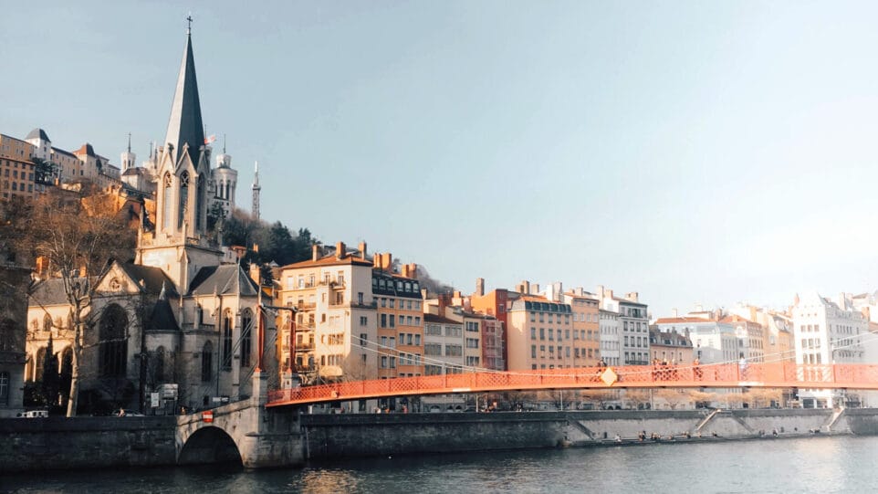 A 19th century church steeple and a golden-red pedestrian bridge line the Saône River in Lyon, France