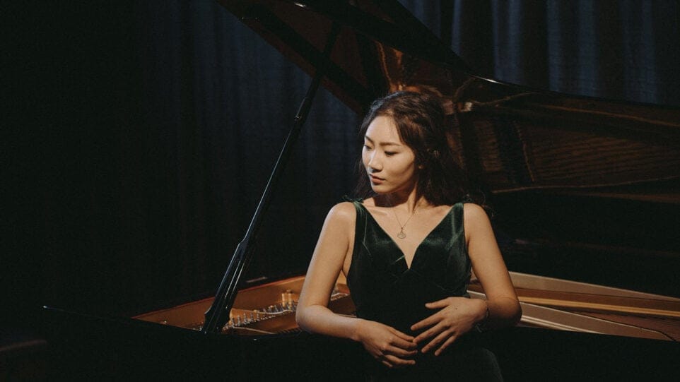 Wynona Wang leans against a moodily lit grand piano