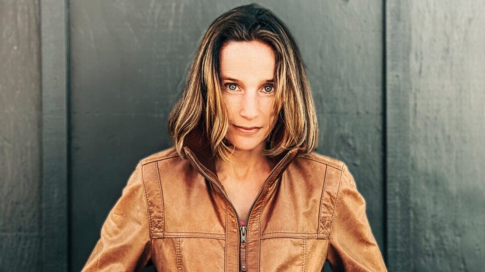 Hélène Grimaud, wearing a brown leather jacket, stands in front of a black wood wall