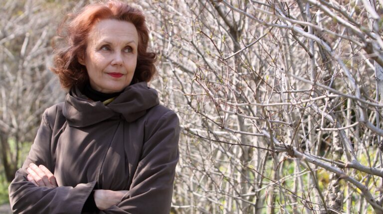 Kaija Saariaho poses against a sunlit thicket