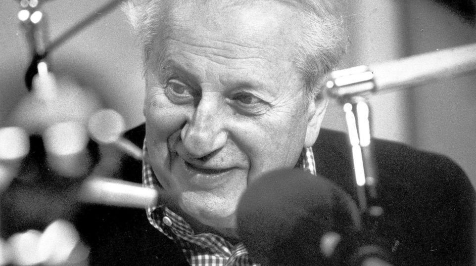 Older man sits in front of a microphone looking interested