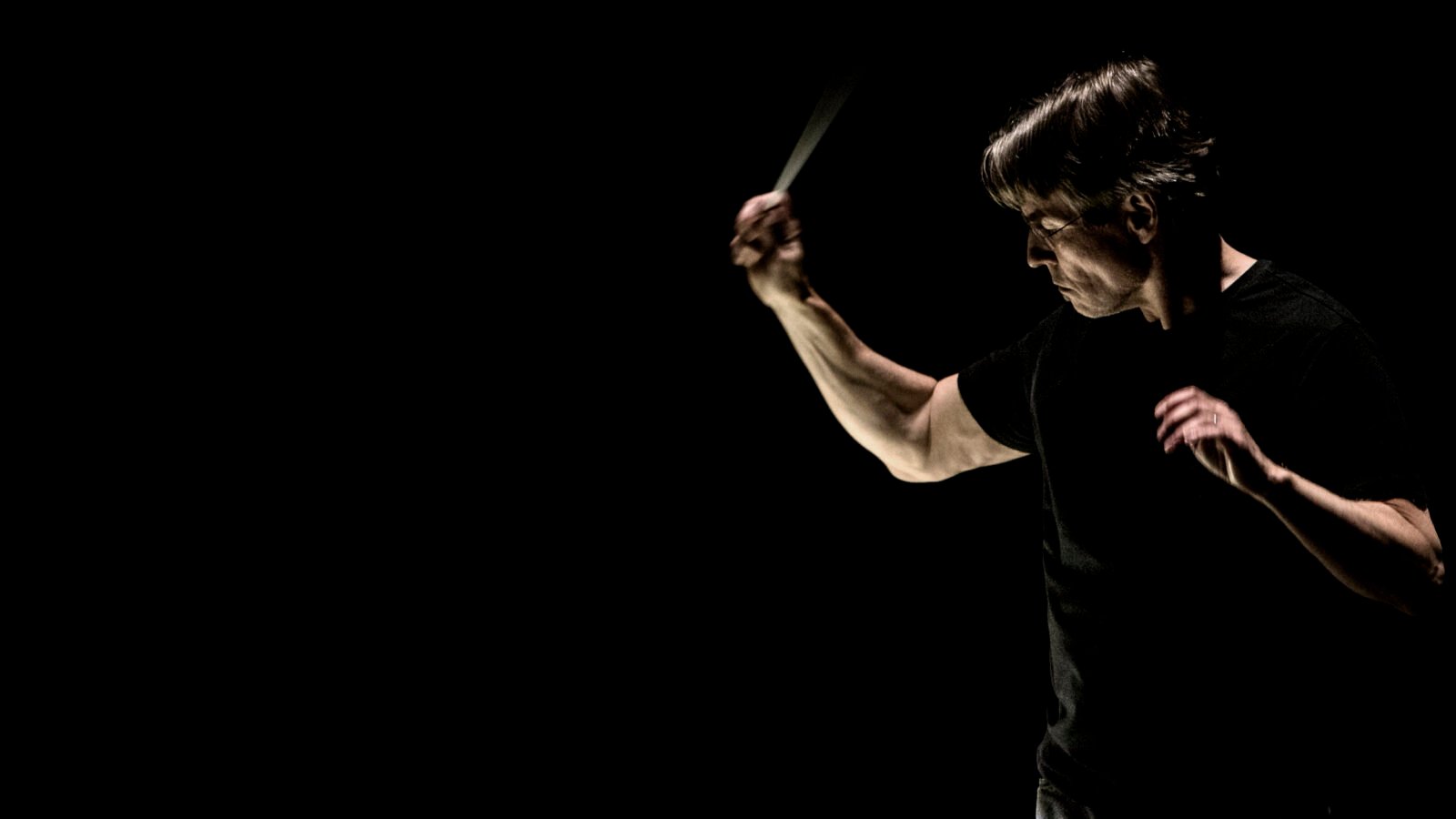 Esa-Pekka Salonen conducting in moody, darkly lit photo